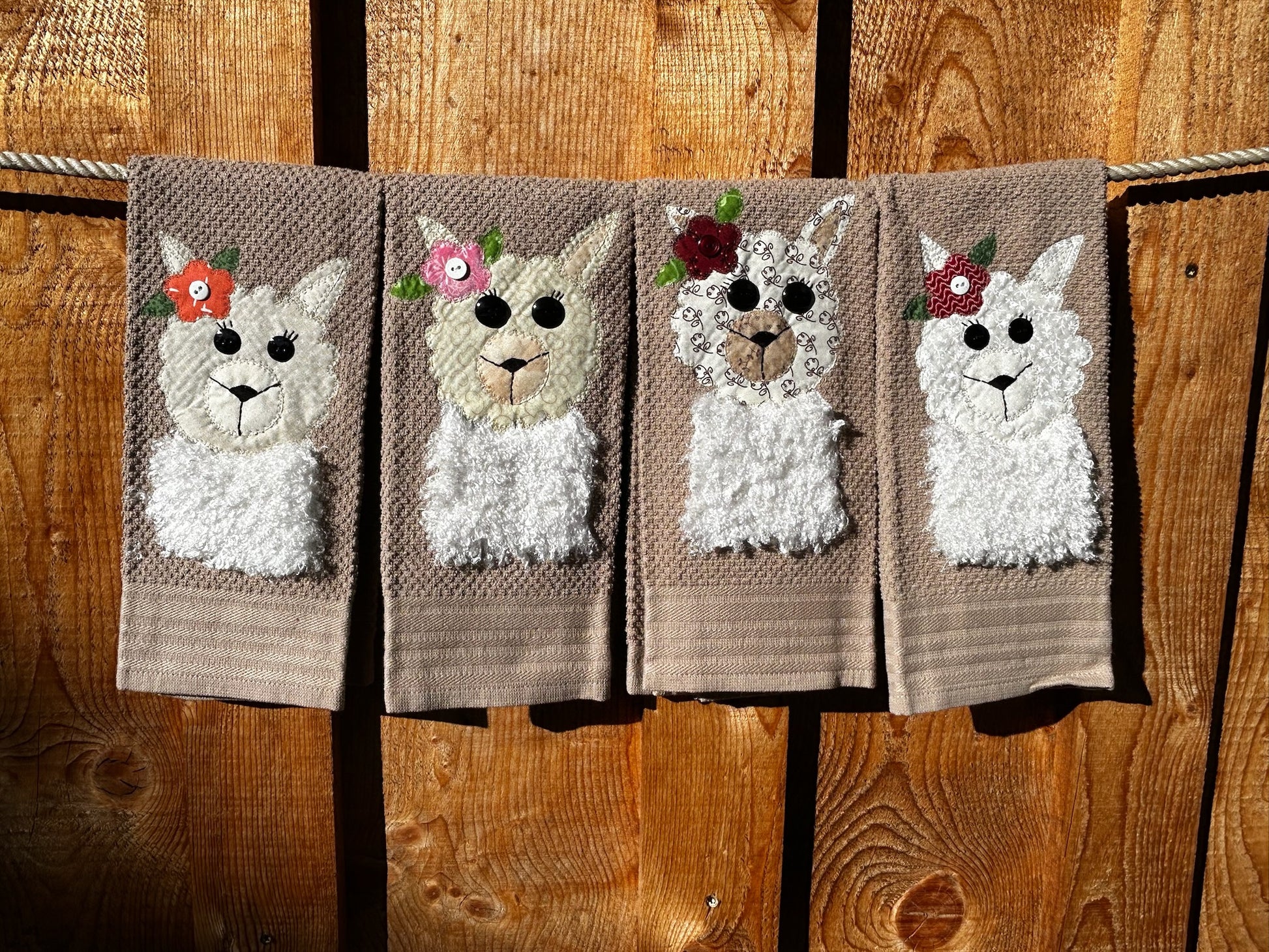 Four dish towels all brown. Each llama is white and fluffy but have a different color and pattern flower on there Left ear