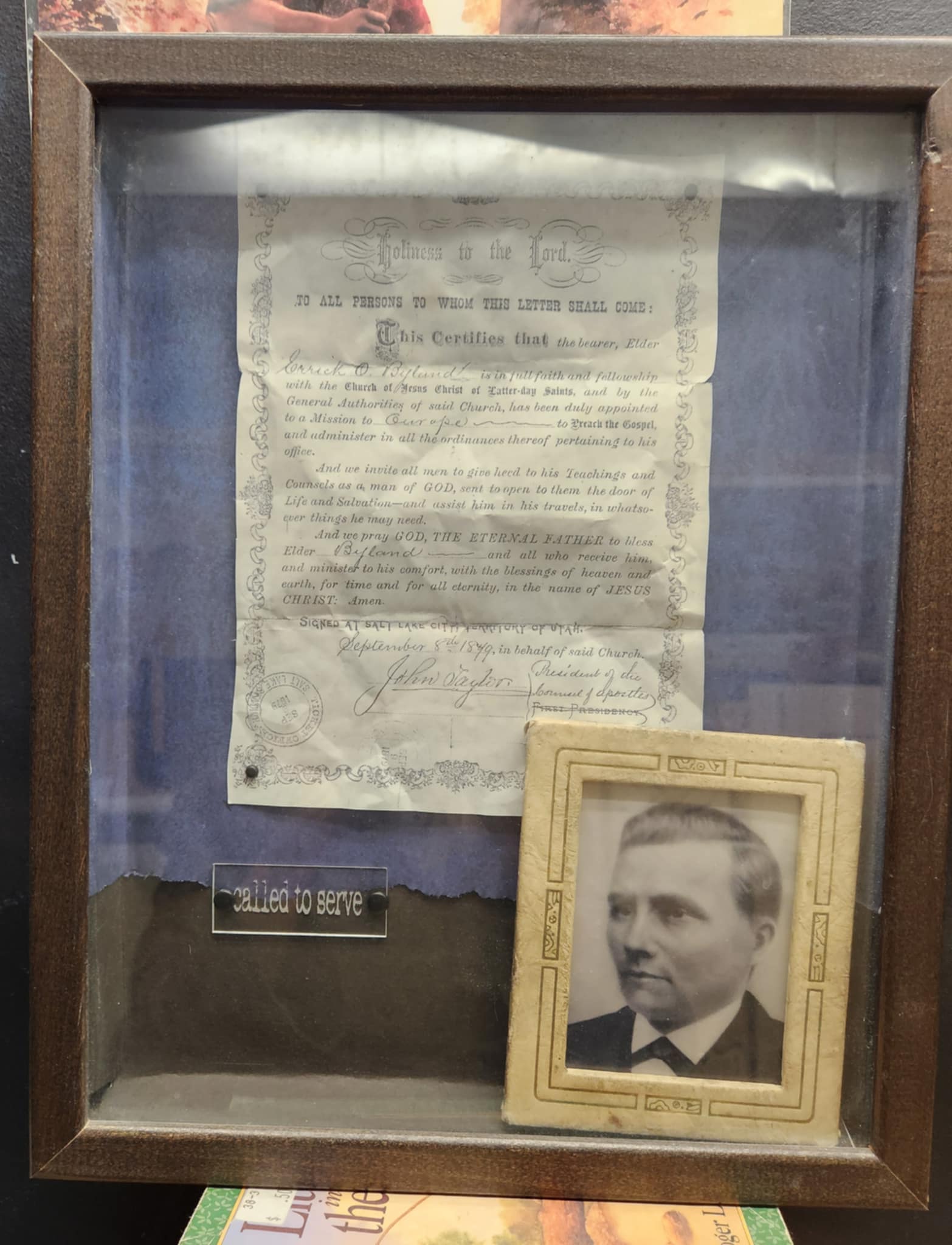 Wood shadow box with a blue background a a paper copy of a mission call  and a photo of the man who got the call