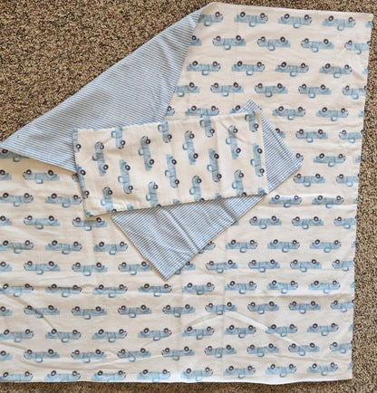 Square Receiving Blanket with Baby blue Pick up trucks with white background Fleece. With corner turned down showing baby blue and white Strip fleece. With tow burp rags  made from the same fabric on top of the blanket