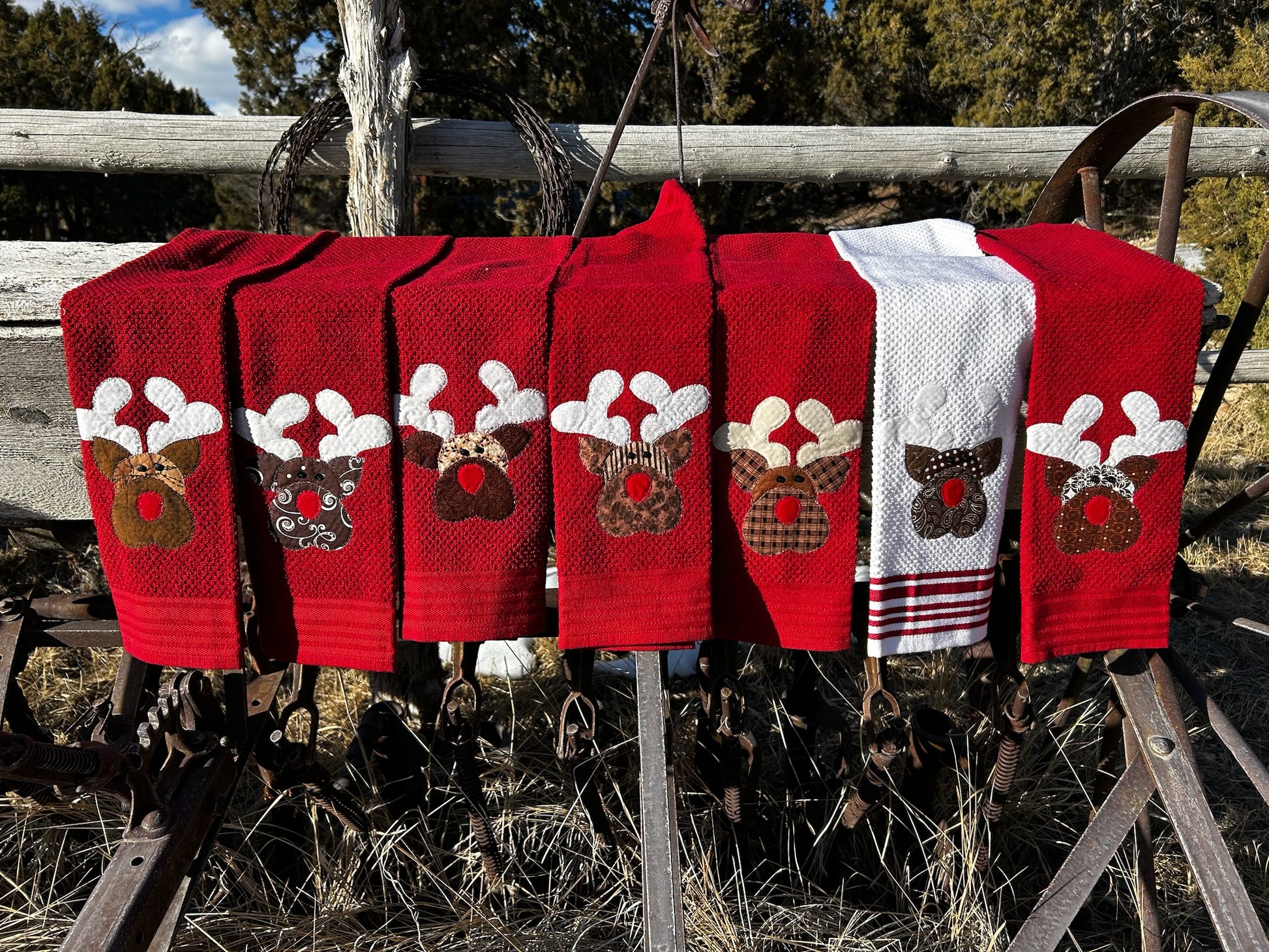 Seven hand towels, six are red and one is white towel. Each red deer has a red nose but each reindeer is brown but different patterns