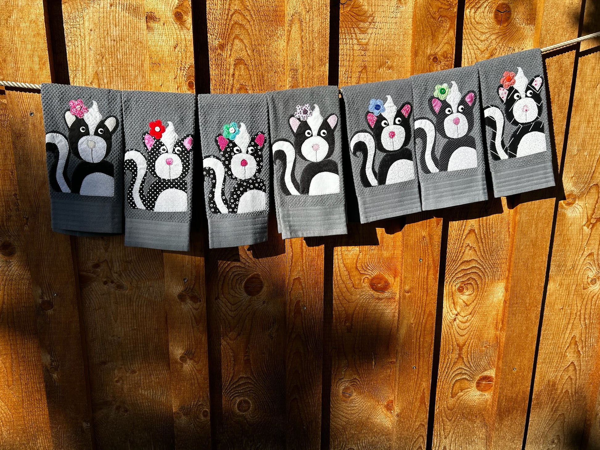 Seven Gray hand towels each skunk is black but different patterns. Each Skunk has a flower on there left ear, each flower is a different color and pattern.