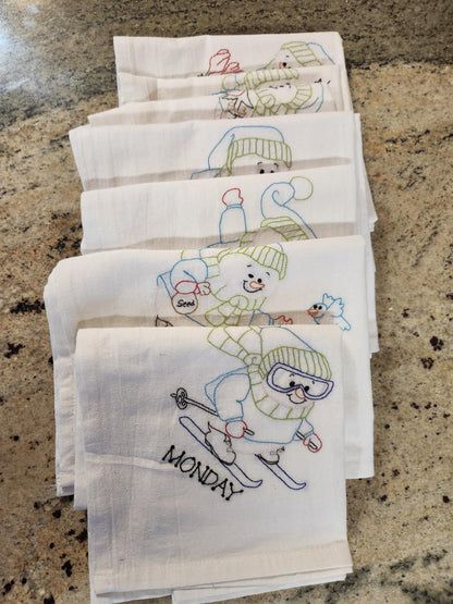 Seven white dish towels folded staggered towels with Snowman Embordered on them.  