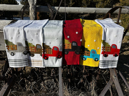 Six hand towels, four white, one red, nd one yellow towel. Each truck is a different color. Each tree is a different color and pattern. Has three white snowflake button above the trucks