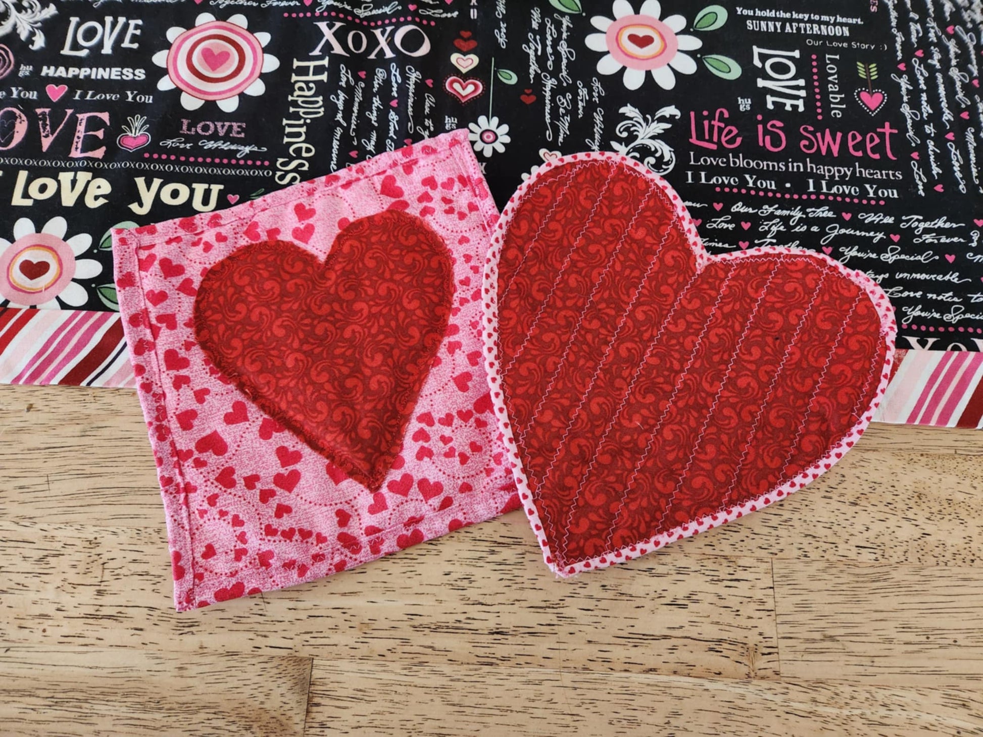 Homemade Valentines Day Heart Hot pads one shaped like a red heart with pink trim and one square hot pad on a pink background and red heart.