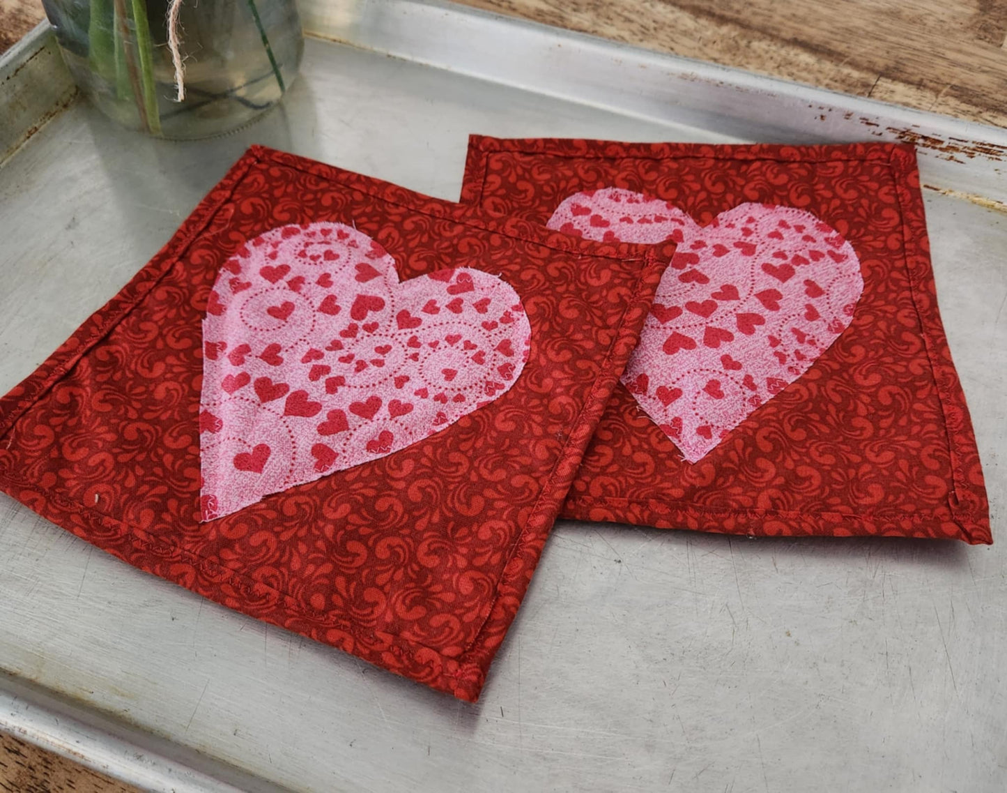 Homemade Valentines Day Heart Hot pads both are square on a red background with a pink heart in the middle.