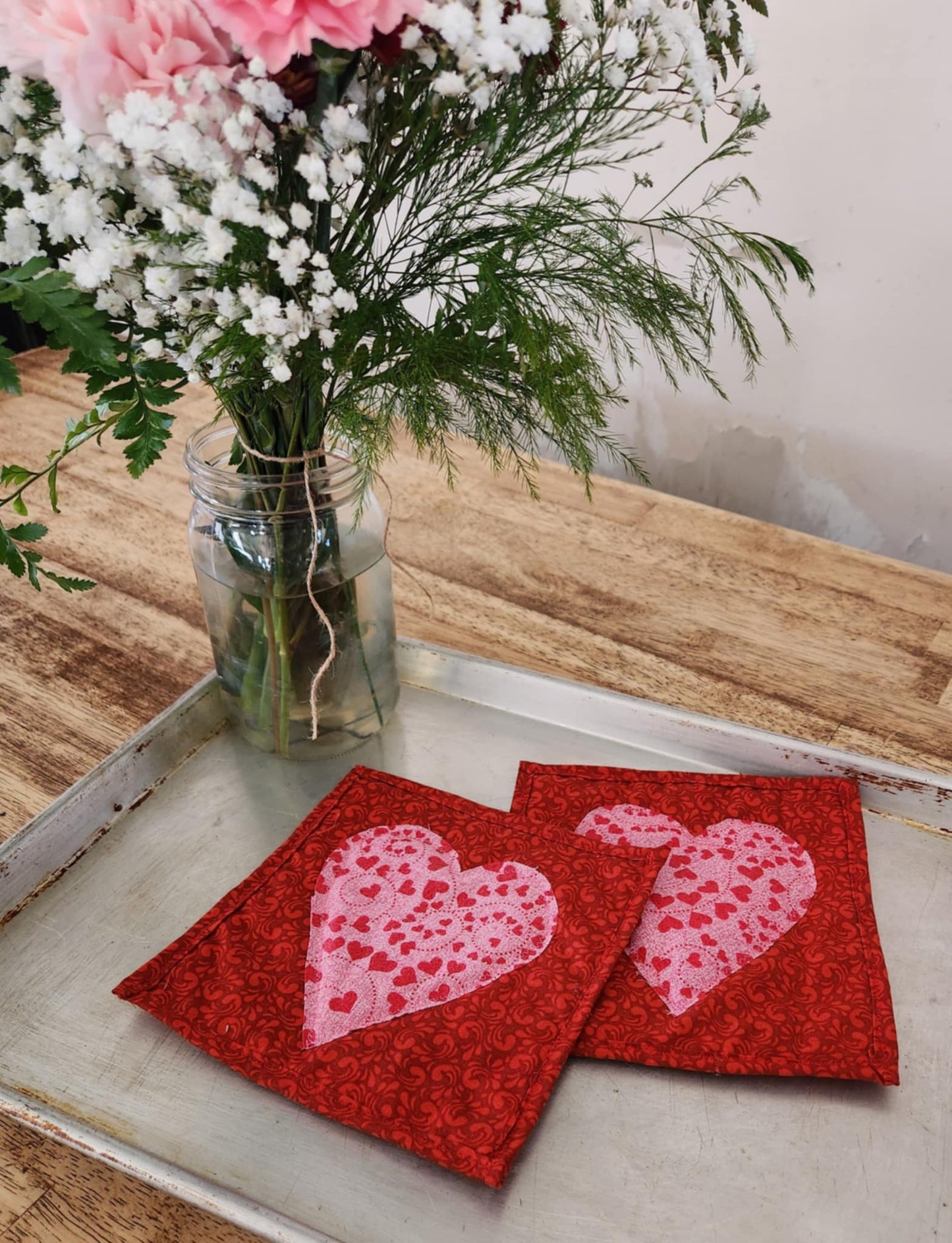 Homemade Valentines Day Heart Hot pads both are square on a red background with a pink heart in the middle.