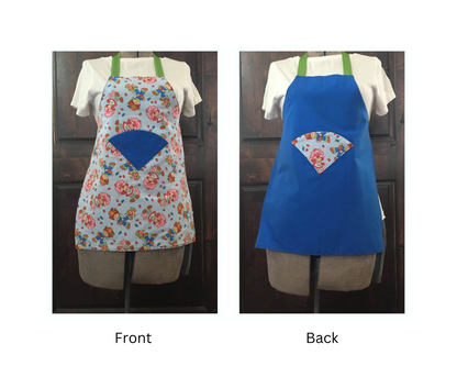 Front and back Kid apron, one with Strawberry short cake with a blue back pattern and a blue pockets in the center,  One apron is displayed frontally and the other is the back showing blue fabric with Strawberry shortcake fabric pocket.  With green ribbon on the top and on both sides to tie
